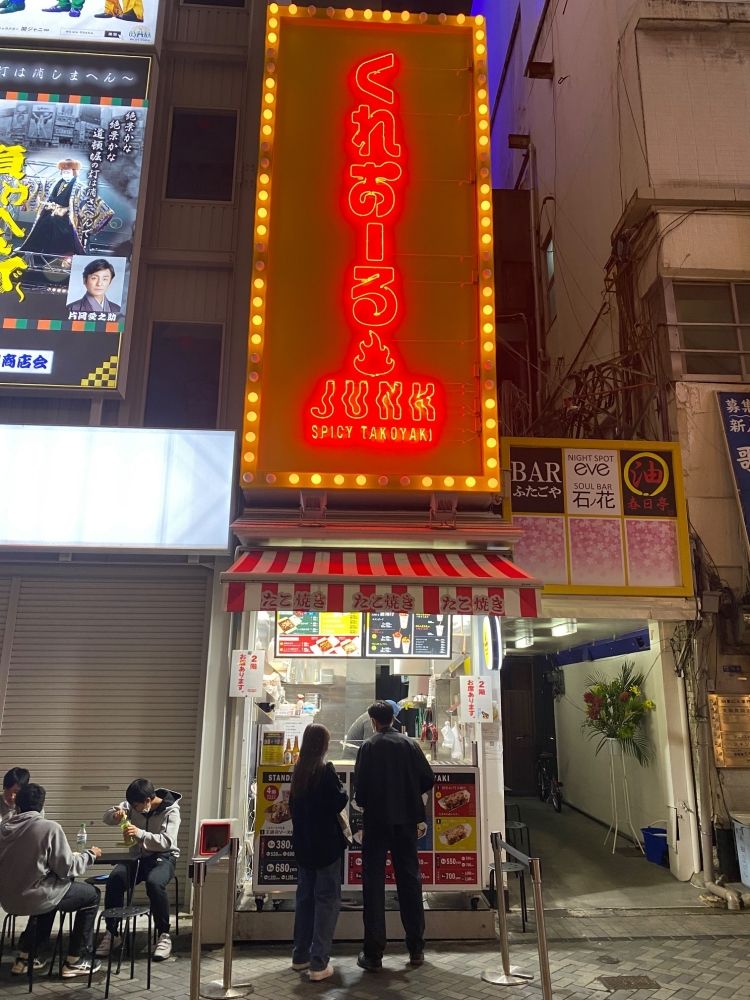 Fazendo takoyaki e tacos em Dotonbori. Por favor, forneça um atendimento ao cliente que faça os turistas estrangeiros sorrirem.